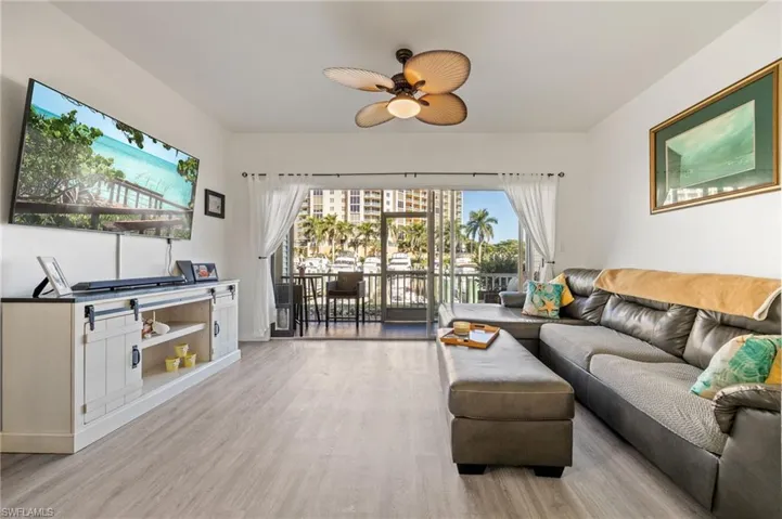 Bright living area featuring wood-finish flooring, a ceiling fan with light fixture, and direct access to a balcony with waterfront scenery