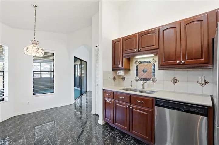 Kitchen featuring dishwasher, arched walkways, hanging light fixtures, tasteful backsplash, and light stone countertops