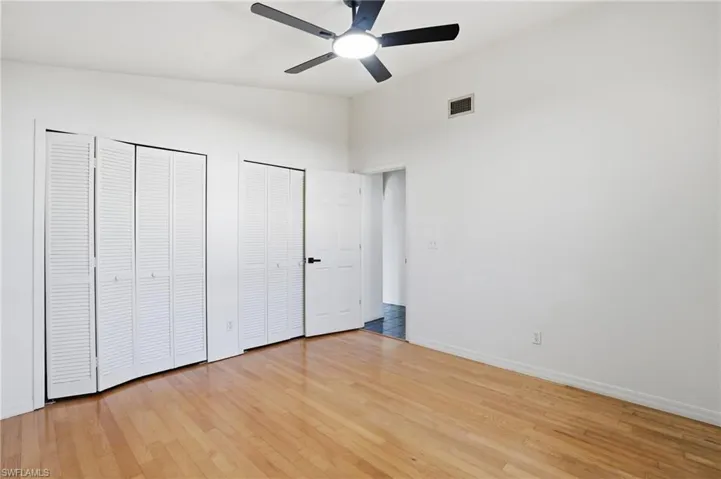 Unfurnished bedroom featuring multiple closets, light wood-style flooring, ceiling fan, and a high ceiling