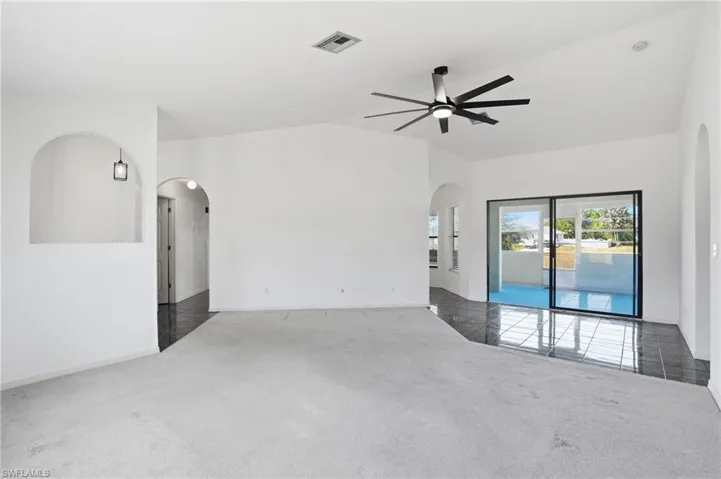 Empty room with carpet flooring, arched walkways, lofted ceiling, and ceiling fan