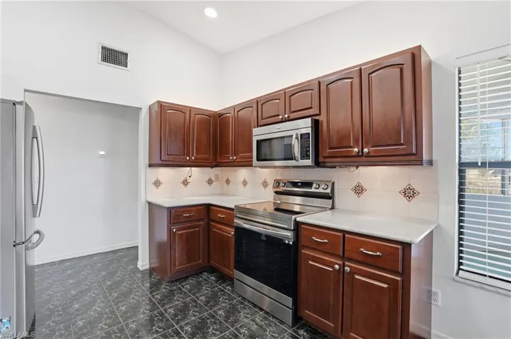 Kitchen with stainless steel appliances, backsplash, dark wood finish cabinetry, recessed lighting, and a high ceiling