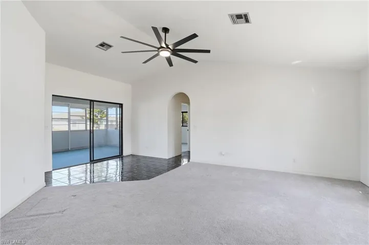 Carpeted empty room with vaulted ceiling, ceiling fan, and arched walkways
