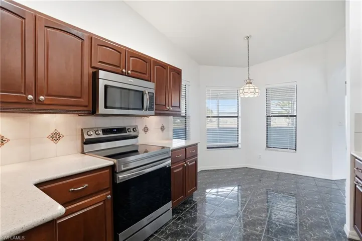 Kitchen featuring stainless steel appliances, pendant lighting, tasteful backsplash, vaulted ceiling, and light stone counters