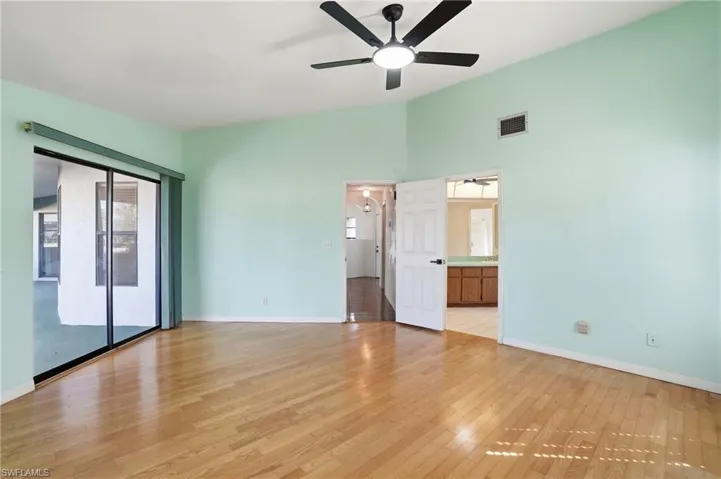 Unfurnished bedroom featuring access to exterior, light wood-style flooring, ceiling fan, ensuite bath, and vaulted ceiling