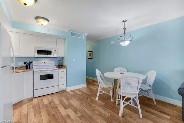 Kitchen with white appliances, decorative light fixtures, light hardwood / wood-style floors, and white cabinets