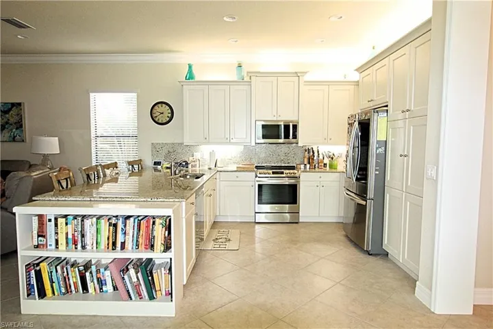 Kitchen with sink, backsplash, appliances with stainless steel finishes, light stone countertops, and crown molding