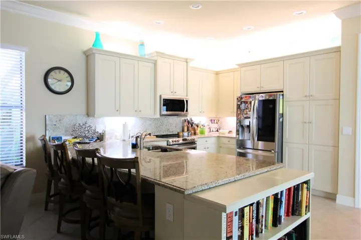 Kitchen featuring kitchen peninsula, a kitchen breakfast bar, appliances with stainless steel finishes, light tile patterned floors, and light stone countertops