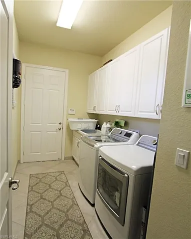 Washroom with light tile patterned floors, independent washer and dryer, and cabinets