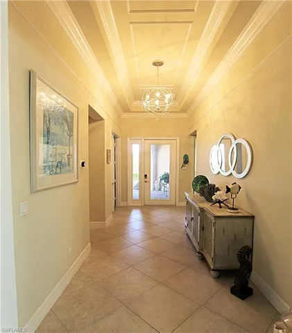 Doorway to outside featuring an inviting chandelier, a raised ceiling, light tile patterned flooring, and crown molding