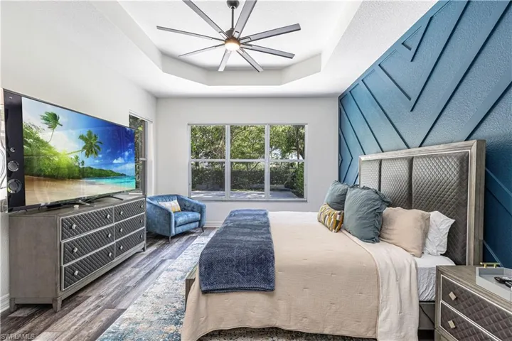 Bedroom with ceiling fan, dark wood-type flooring, and a tray ceiling