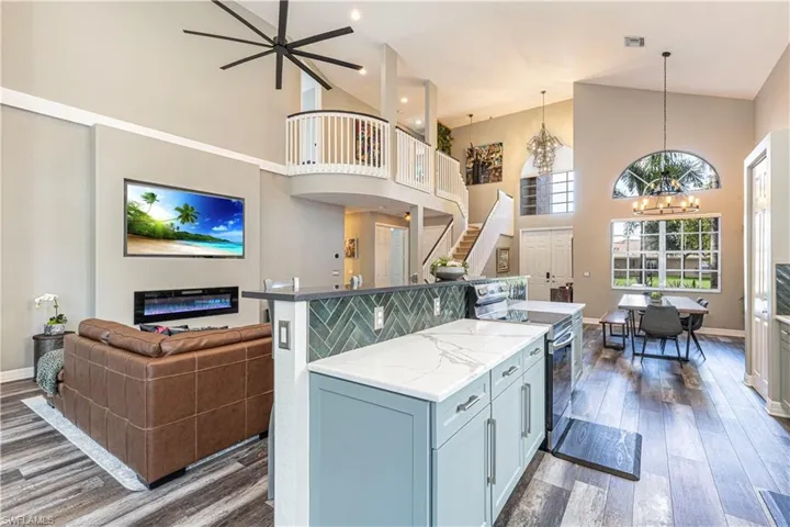 Kitchen featuring dark wood-type flooring, light stone counters, hanging light fixtures, a towering ceiling, and stainless steel range with electric stovetop