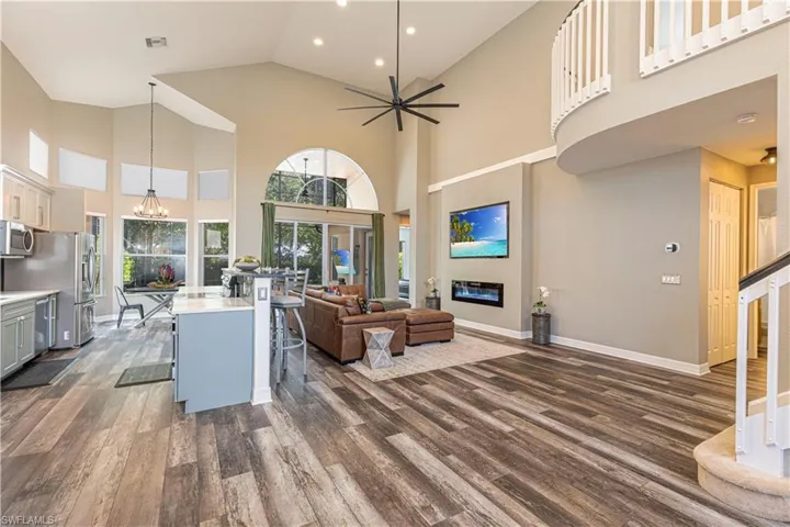 Living room featuring high vaulted ceiling, ceiling fan with notable chandelier, and dark hardwood / wood-style flooring