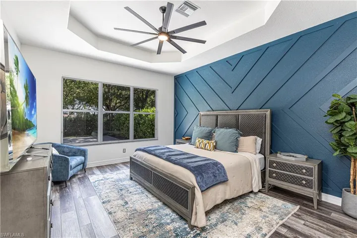 Bedroom with dark hardwood / wood-style floors, ceiling fan, and a raised ceiling