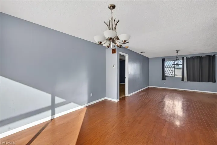 Unfurnished room featuring a chandelier, a textured ceiling, and dark wood-style flooring
