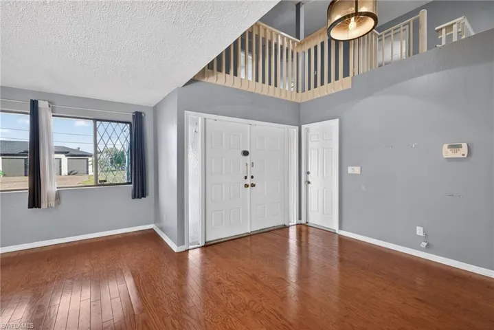 Foyer entrance with wood-type flooring, a textured ceiling, and a high ceiling