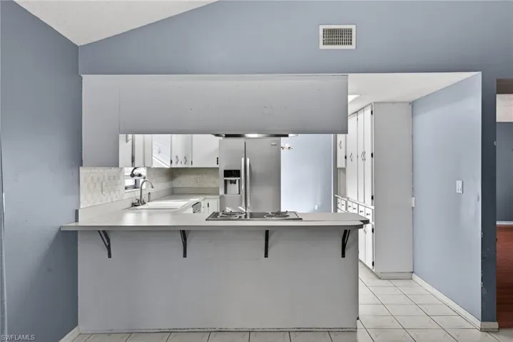 Kitchen featuring light countertops, white cabinets, a kitchen breakfast bar, appliances with stainless steel finishes, and vaulted ceiling