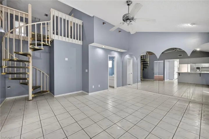 Unfurnished living room with stairs, light tile patterned flooring, ceiling fan, arched walkways, and high vaulted ceiling