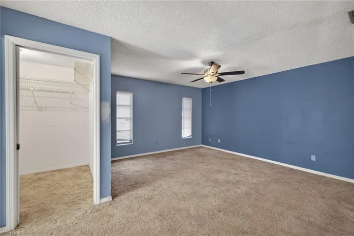 Unfurnished bedroom with a spacious closet, carpet flooring, a textured ceiling, and ceiling fan