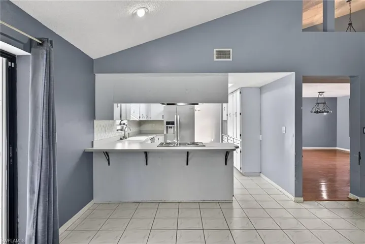Kitchen featuring light countertops, a breakfast bar area, vaulted ceiling, stainless steel appliances, and white cabinets