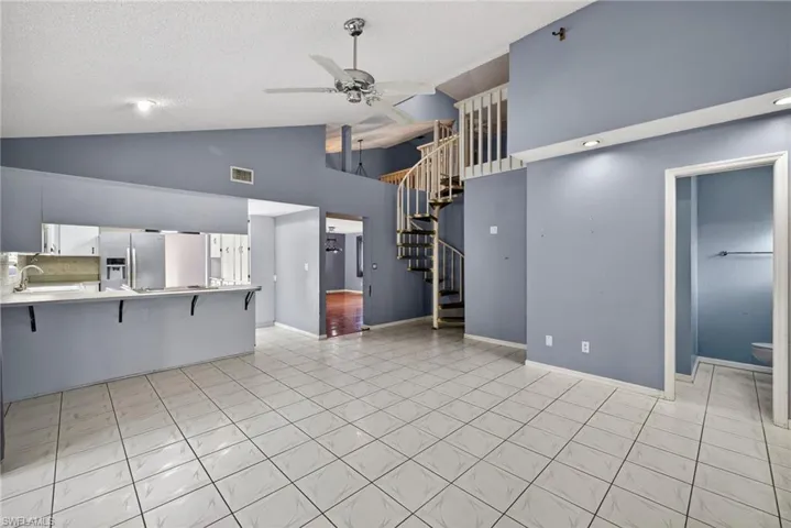 Unfurnished living room with ceiling fan, light tile patterned flooring, stairway, a textured ceiling, and high vaulted ceiling