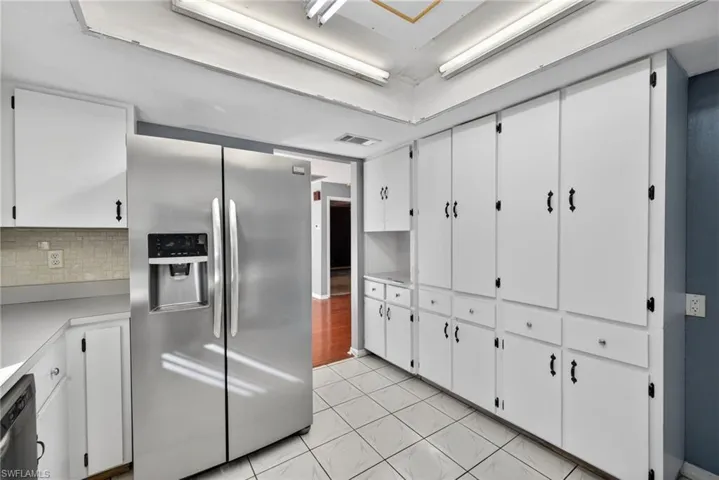 Kitchen with stainless steel fridge with ice dispenser, white cabinets, light countertops, tasteful backsplash, and dishwashing machine
