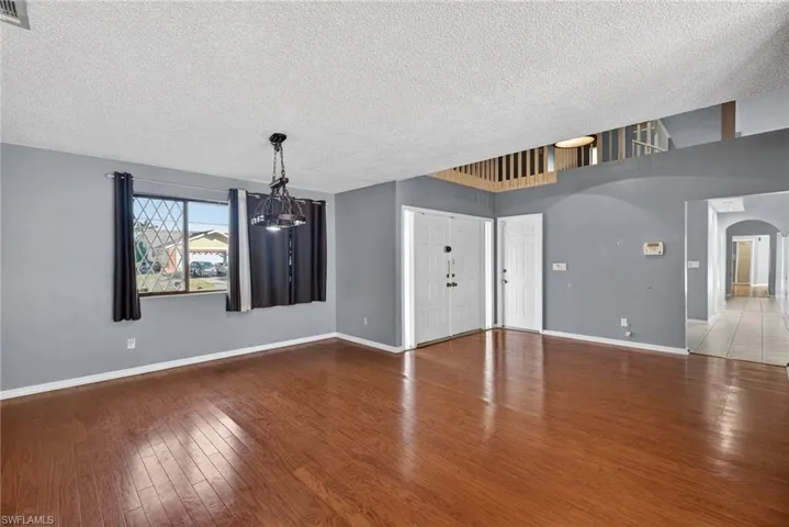 Unfurnished living room with hardwood / wood-style floors, a textured ceiling, arched walkways, and a chandelier