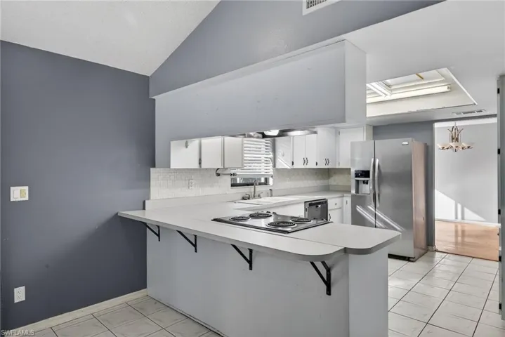 Kitchen featuring light countertops, a kitchen breakfast bar, appliances with stainless steel finishes, a peninsula, and lofted ceiling