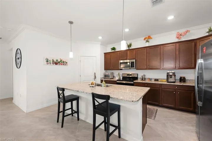 Spacious kitchen featuring an expansive island with seating, pendant lighting, built-in stainless steel microwave, and wood-finish cabinetry