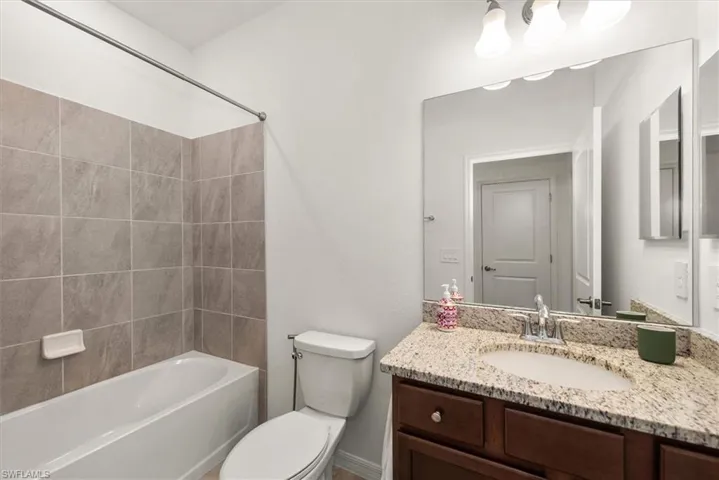 Full bathroom featuring a tub-shower combination with tiled surround, a toilet, a vanity with a granite-finish countertop, an integrated sink with chrome faucet, and a large mirror