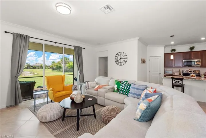 Living area featuring expansive sliding glass doors, tile flooring, crown molding, and an open-concept layout with a visible kitchen bar