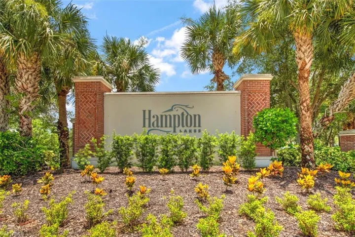 Entry monument with a brick and stucco finish, featuring surrounding tropical landscaping, palm trees, and varied shrubbery