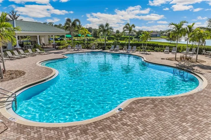 The property features a large, irregularly shaped swimming pool with a brick paver deck, surrounded by palm trees and lounge chairs