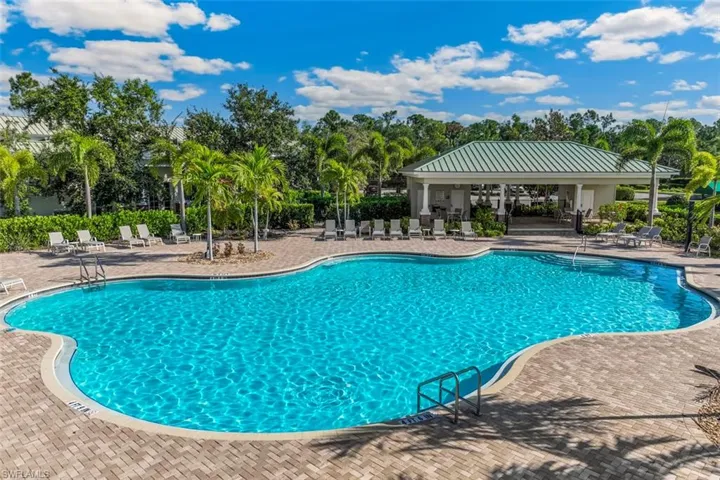 This property features an expansive outdoor pool area with clear blue water, surrounded by a paver patio and lounge chairs