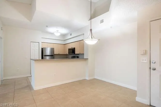Kitchen featuring decorative light fixtures, light brown cabinets, kitchen peninsula, appliances with stainless steel finishes, and light tile floors
