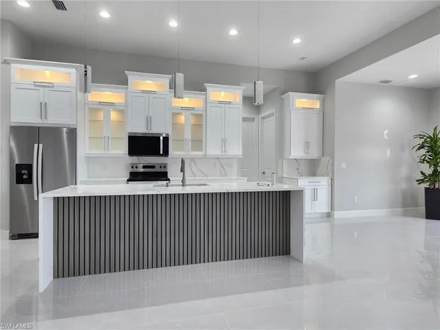 Kitchen with pendant lighting, stainless steel appliances, an island with sink, and white cabinetry