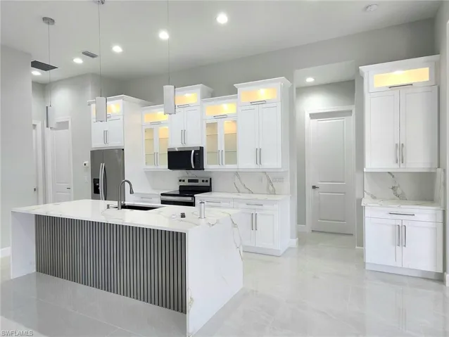 Kitchen featuring an island with sink, appliances with stainless steel finishes, hanging light fixtures, and white cabinetry