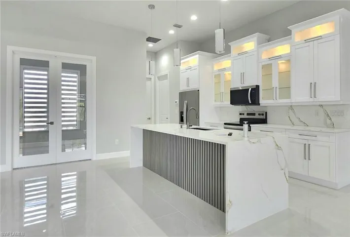 Kitchen featuring appliances with stainless steel finishes, hanging light fixtures, an island with sink, and white cabinets