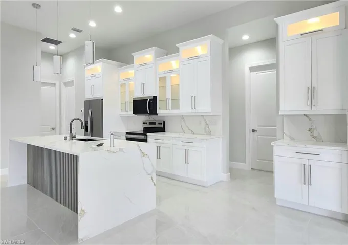 Kitchen with white cabinetry, decorative light fixtures, appliances with stainless steel finishes, and a kitchen island with sink