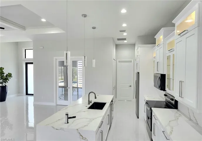 Kitchen with a kitchen island with sink, sink, white cabinetry, hanging light fixtures, and stainless steel appliances