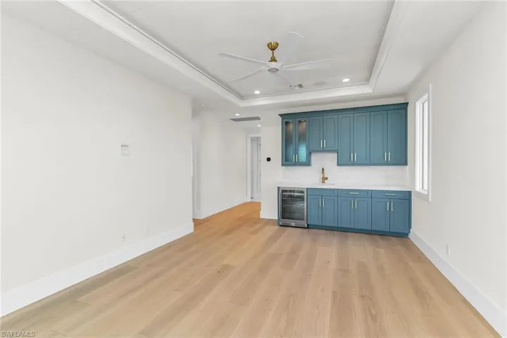 Unfurnished living room featuring light wood-type flooring, wet bar, a ceiling fan, a raised ceiling, and wine cooler