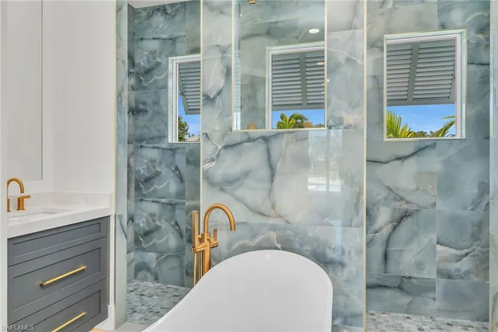 Full bath with a freestanding tub, vanity, and a marble finish shower
