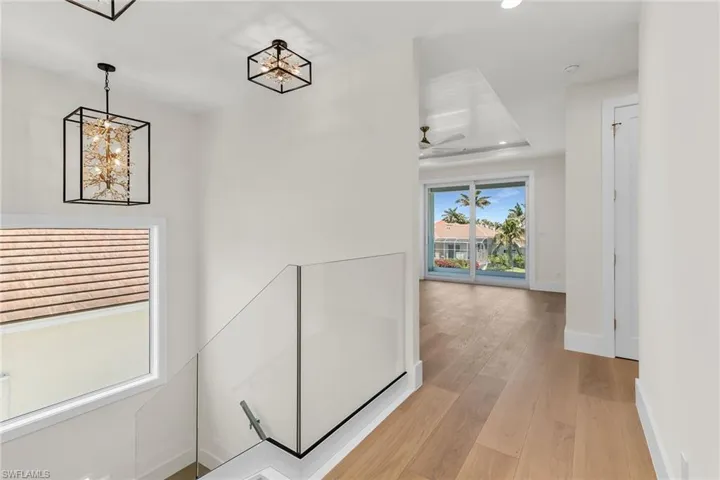 Hall with light wood-style flooring, a tray ceiling, recessed lighting, a notable chandelier, and baseboards