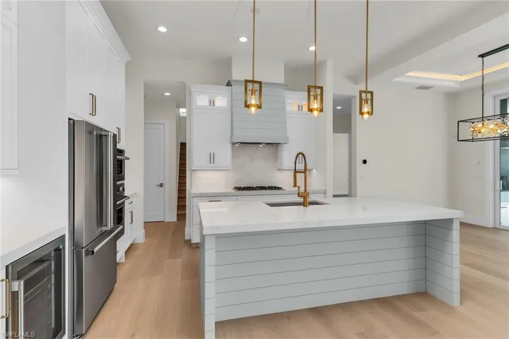 Kitchen featuring light wood-style flooring, appliances with stainless steel finishes, a sink, wine cooler, and backsplash