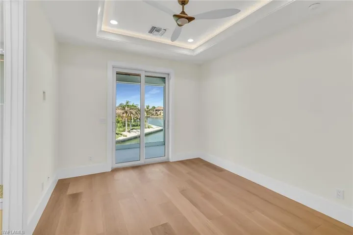 Empty room featuring a tray ceiling, light wood-type flooring, baseboards, and a ceiling fan