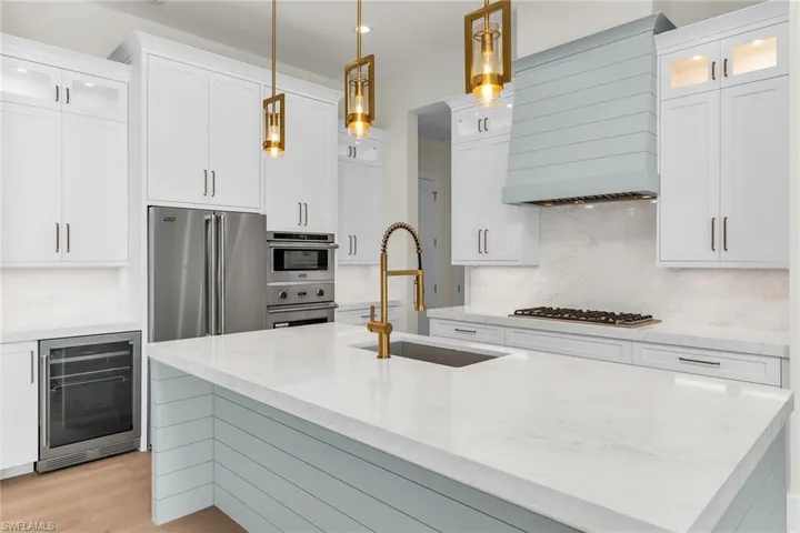 Kitchen with white cabinets, a sink, stainless steel appliances, wine cooler, and decorative backsplash