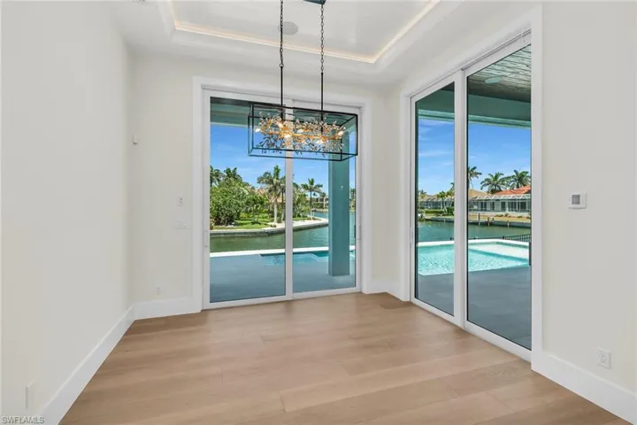 Unfurnished dining area featuring a notable chandelier, baseboards, light wood-style floors, a tray ceiling, and a water view