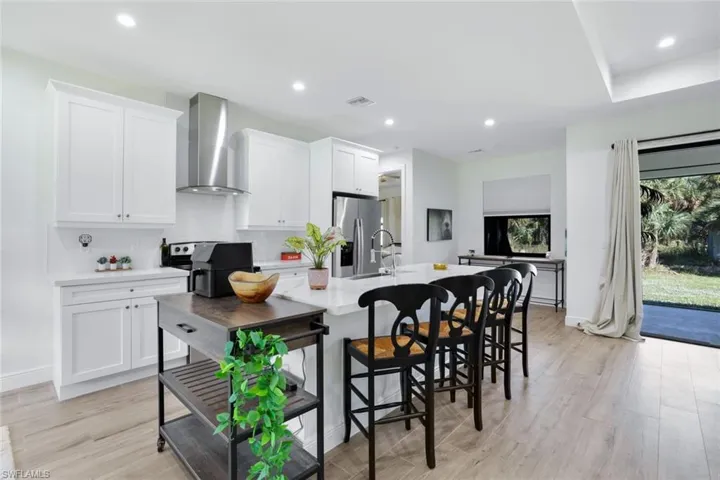 Kitchen with black / electric stove, white cabinets, wall chimney exhaust hood, and light hardwood / wood-style floors