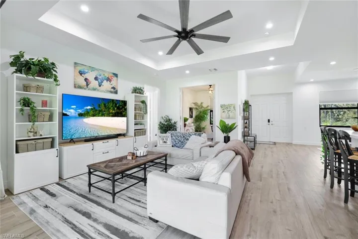 Living room with ceiling fan, light wood-type flooring, and a tray ceiling