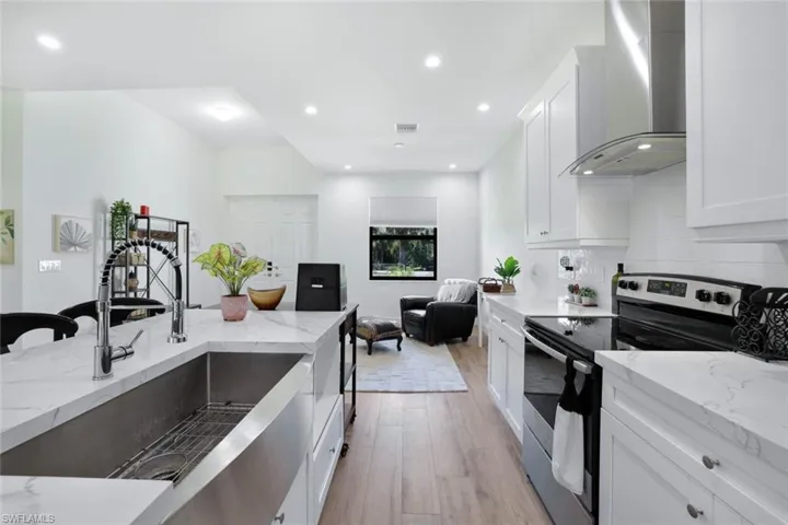 Kitchen with light stone counters, wall chimney range hood, white cabinets, light hardwood / wood-style floors, and stainless steel range with electric cooktop