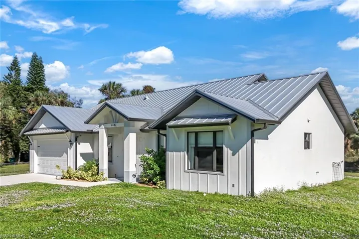 Modern farmhouse with metal roof, an attached garage, concrete driveway, board and batten siding, and a front yard
